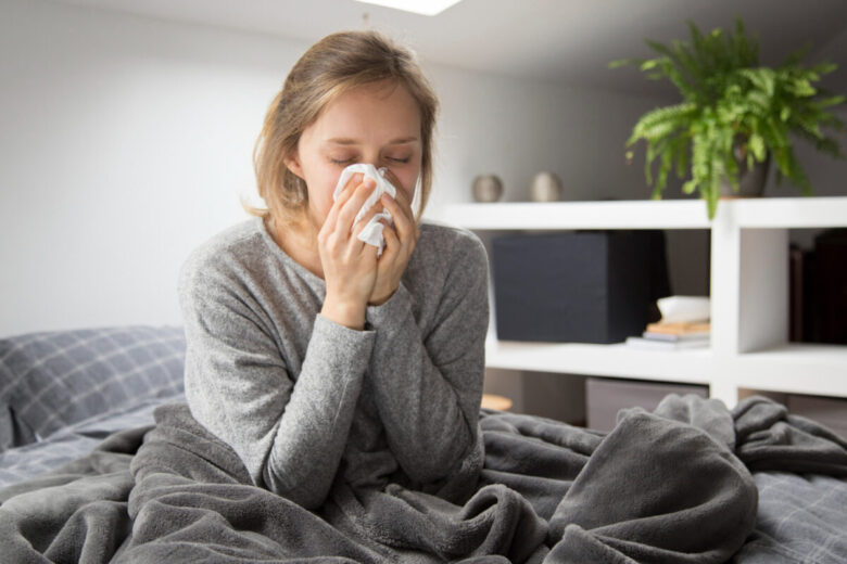 sick-woman-sitting-bed-blowing-nose-with-napkin